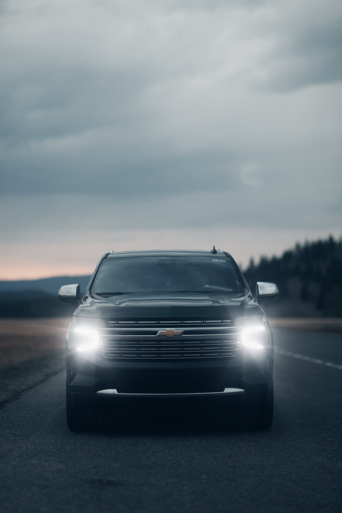 A black Chevrolet Tahoe SUV driving on an empty road during dusk, with headlights on.